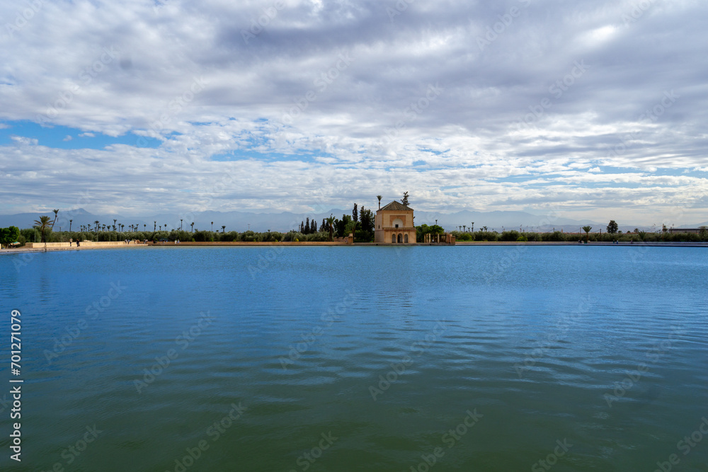 Photo of the Menara Gardens in the city of Marrakech. Photo of the lake with the house at the end of the lake. The house reflected in the lake. Cloudy day.