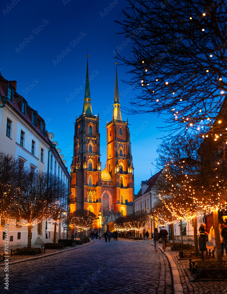 Street with cobblestone road, lights on trees, St. John the Baptist Cathedral with two spiers in the old historical city center, Tumski Island, Wroclaw, Poland