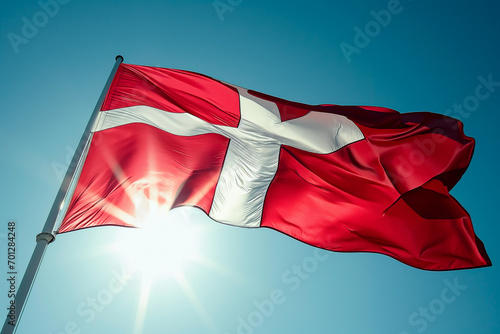 Danish flag against the sun in a clear sky.
 photo