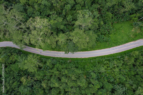 Aerial view of a road in the middle of the green forest and road curve construction up to mountain.