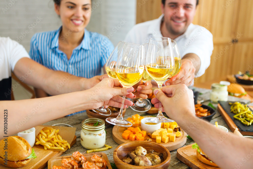 People with white wine toasting over served table with food. People with white wine toasting over served table with food.