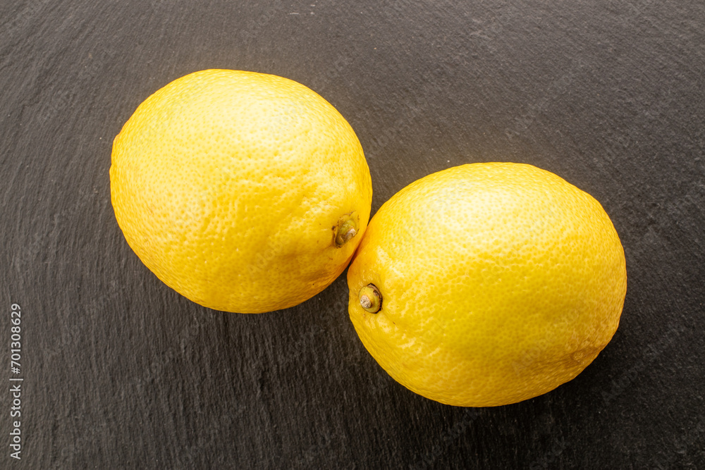 Two yellow ripe lemons on a slate board, close-up, top view.