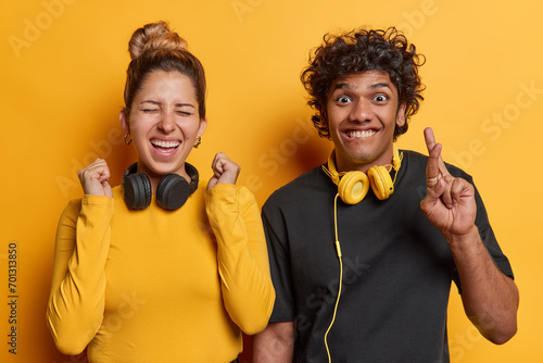 People and happiness. Studio waist up of young happy smiling excited European woman and Hindu guy standing close to each other on yellow background wearing casual clothes with headphones on neck photo