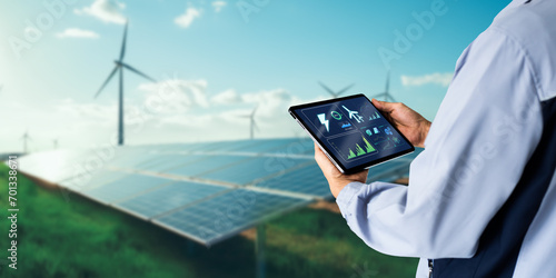 Sustainable energy management system concept.Engineer using digital tablet with wind turbine and solar panels powerplant as background photo