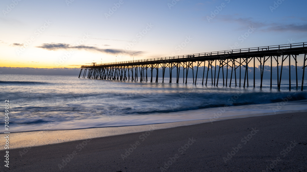 Sunrise casts a warm glow over Kure Beach pier, with soft waves lapping the shore in North Carolina. Sunrise casts a warm glow over Kure Beach pier, with soft waves lapping the shore in North Carolina.