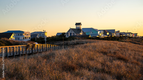 Sunrise illuminates a boardwalk and coastal houses in Oak Island, North Carolina, with the golden sky in the background.