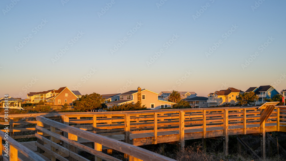 Sunrise illuminates a boardwalk and coastal houses in Oak Island, North Carolina, with the golden sky in the background.