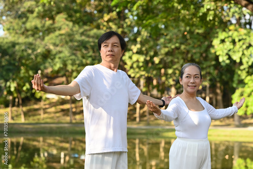 Active middle age couple in white clothing working out with Tai Chi in the park. Health care and wellbeing concept. © Prathankarnpap