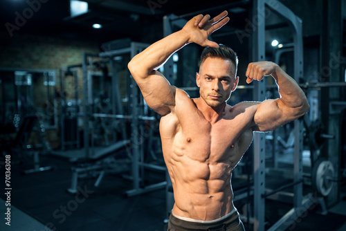 young athletic bodybuilder sportsman posing with torso in gym after workout