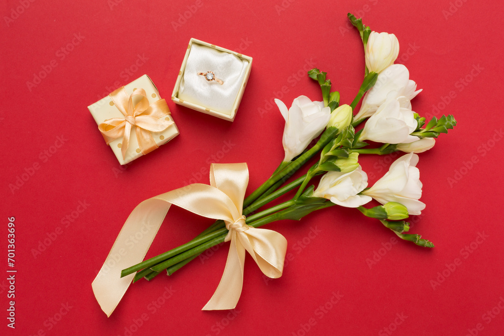 White freesia flower and gift box with diamond ring on color background, top view White freesia flower and gift box with diamond ring on color background, top view