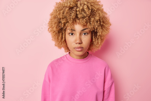 People positive emotions concept. Studio waist up of young happy pretty fit European female standing in centre isolated on pink background wearing sweater keeping hands down calm and relaxed photo