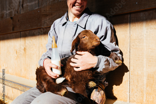 Crop of happy woman after feeding adorable lamb with milk bottle in barn