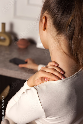 Close up of woman hand on shoulder, suffering from muscle neck pain in home workplace. Moody young lady holding her neck and injury at living room. Healthcare and medical concept. Copy ad text space