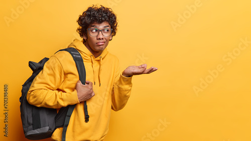 People emotions concept and student lifestyle. Indoor waist up of young disappointed Hindu guy standing on left isolated on yellow background with bag looking at blank space for your advertisement © wayhome.studio 