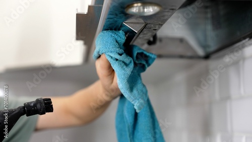 Woman wiping exhaust hood in kitchen, closeup. A woman's hand washes the hood in the kitchen with a rag. Cleaning a household hood. Female hands cleaning a kitchen hood with a cloth.