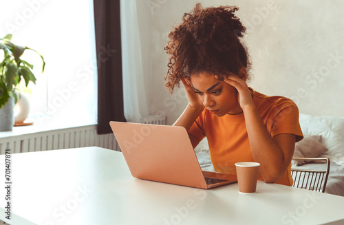 Frustrated African descent young woman in front of laptop at home, receiving e-mail with bad news photo