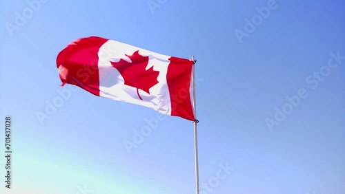 Canadian flag flapping in wind on blue sky.