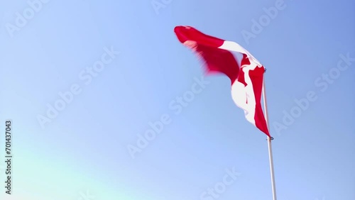 Canadian flag flapping in wind on blue sky.