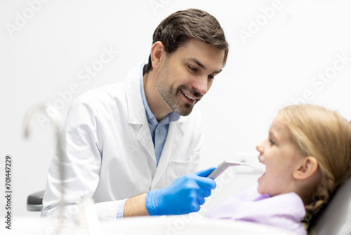 Male dental professional hiding dental pneumatic spray gun  preparing for dental treatment for child girl in clinic  side view