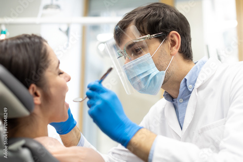 Man dentist in face mask and glasses doing treatment for female patient, holding dental tools, wearing rubber gloves. Modern dental clinic concept