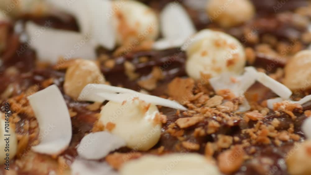 Close up. Food goes from clear to blurred. Chocolate pizza on a pink plate on a white background swirls together with the ingredients of mascarpone, hazelnuts, coconut shavings, and cream. Close up. Food goes from clear to blurred. Chocolate pizza on a pink plate on a white background swirls together with the ingredients of mascarpone, hazelnuts, coconut shavings, and cream.