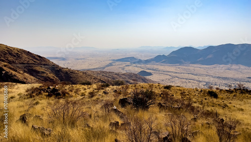 Namib-Naukluft National Park, Namibia - August 24, 2022: Expansive view of a rugged Namibian landscape featuring rolling hills, grassy plains, and distant mountains under a hazy blue sky