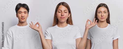 Image of three mixed race people dressed in basic casual t shirts pose against white background in studio. European woman meditates and practices yoga poses between Japanese man calm brunette female photo