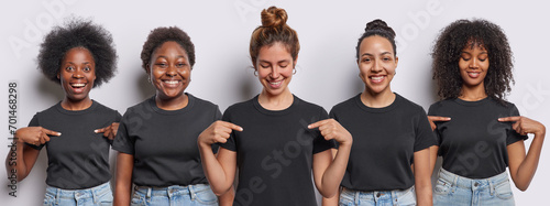 Waist up shot of cheerrful women stand in row point at blank space of casual t shirts show place for your advertising logo or text wear jeans isolated over white background. People clothing template
