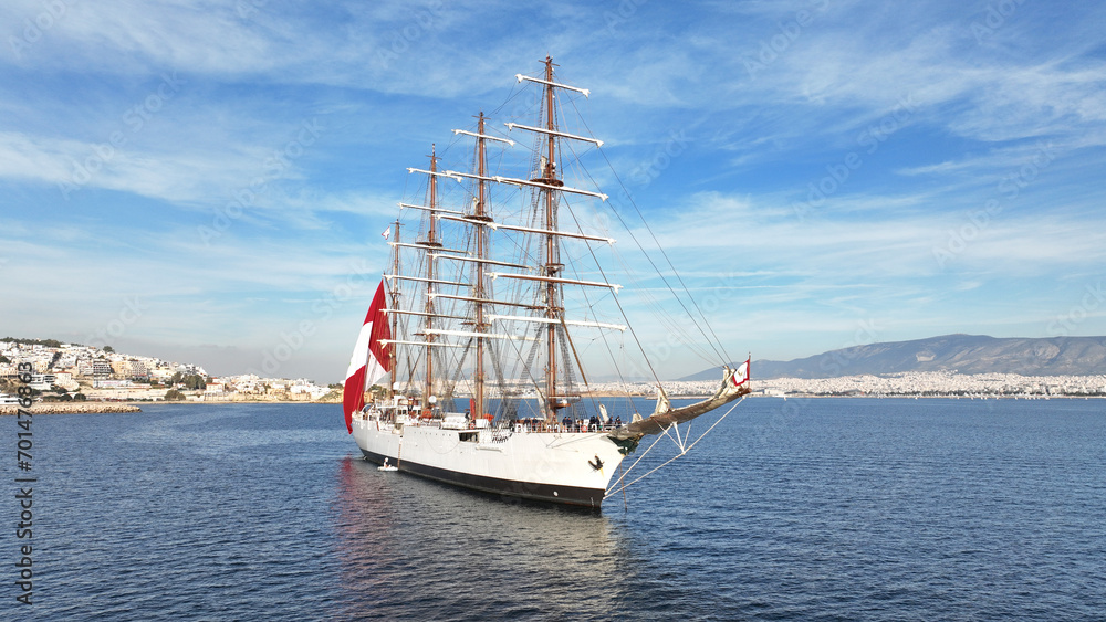 Aerial drone photo of beautiful 3 mast barque or barc type classic sailing wooden boat with huge waving flag anchored near port of Piraeus, Attica, Greece