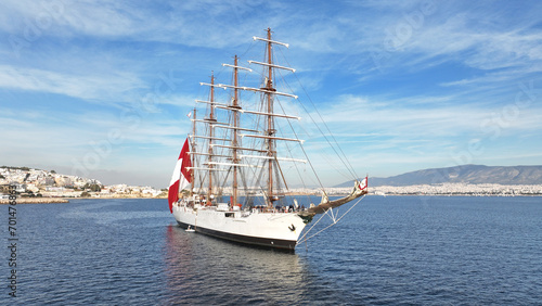 Aerial drone photo of beautiful 3 mast barque or barc type classic sailing wooden boat with huge waving flag anchored near port of Piraeus, Attica, Greece