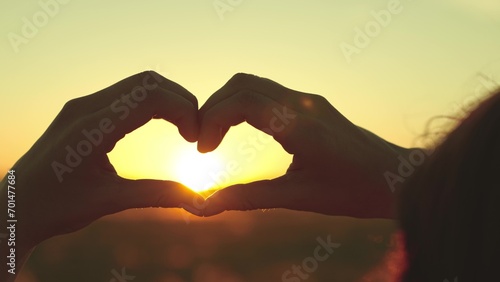 Traveller expresses love for Earth through heart-shaped gesture at sunset. Traveller comes to park after work to spend evening watching sunset. Traveller waits for night in field to look at stars