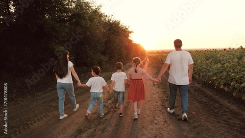 Large family with children walks holding hands along rural road at sunset. Parents with children enjoy walking in summer park on family vacation. Little children and parents walk together