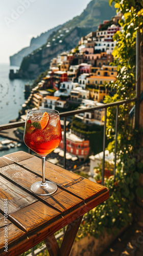 Glass of aperol spritz on a wooden table on a balcony overlooking Positano Italy on a sunny day with italian buildings in the background prompting desire to drink the glass and travel © Sophie 