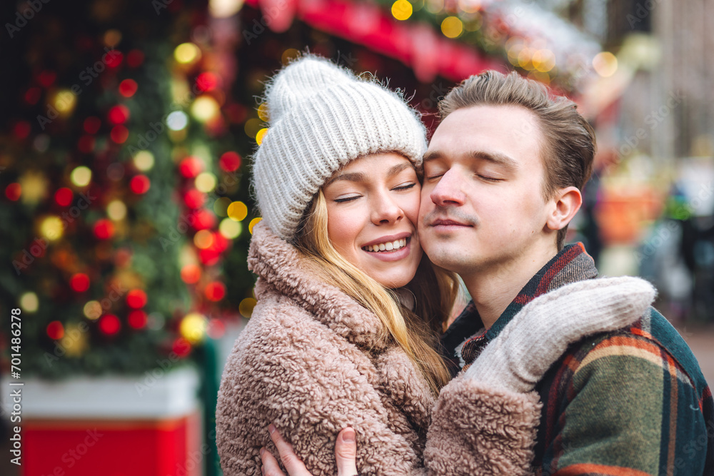 Portrait of young loving happy beautiful couple having fun enjoying decorated Xmas market. Kiss, hug, embrace each other, precious magic moments together on holiday time. Warm clothes, snow Portrait of young loving happy beautiful couple having fun enjoying decorated Xmas market. Kiss, hug, embrace each other, precious magic moments together on holiday time. Warm clothes, snow