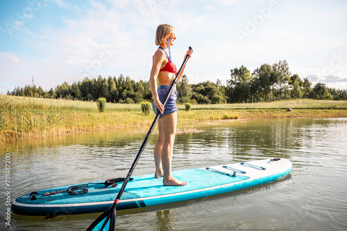 Young woman with athletic body shape swimming on sup board with long paddle in hands.