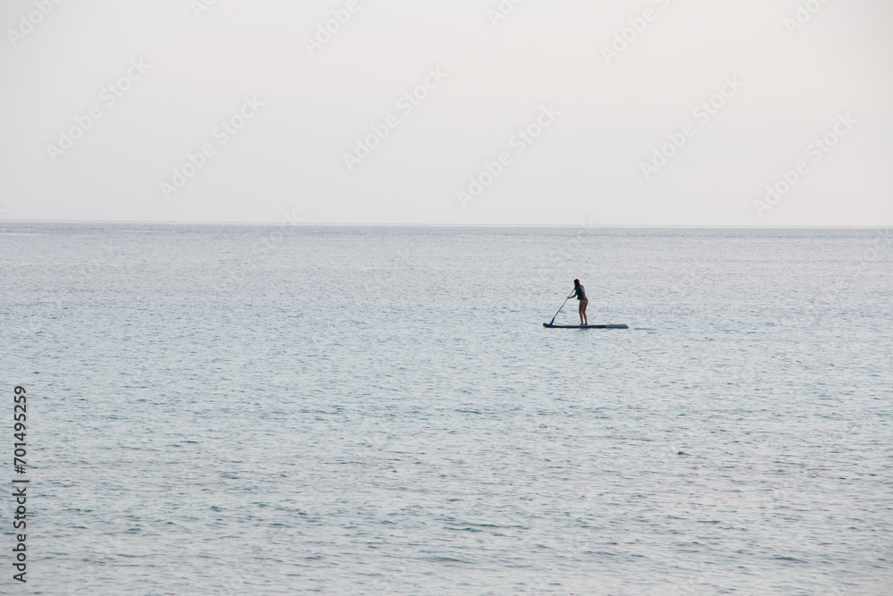 Naklejka premium An unrecognizable woman in the distance, paddle surfing completely alone in a calm sea