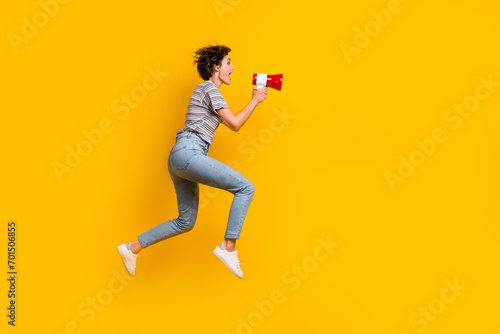 Full size profile portrait of astonished girl hold communicate toa loudspeaker jump run empty space isolated on yellow color background photo