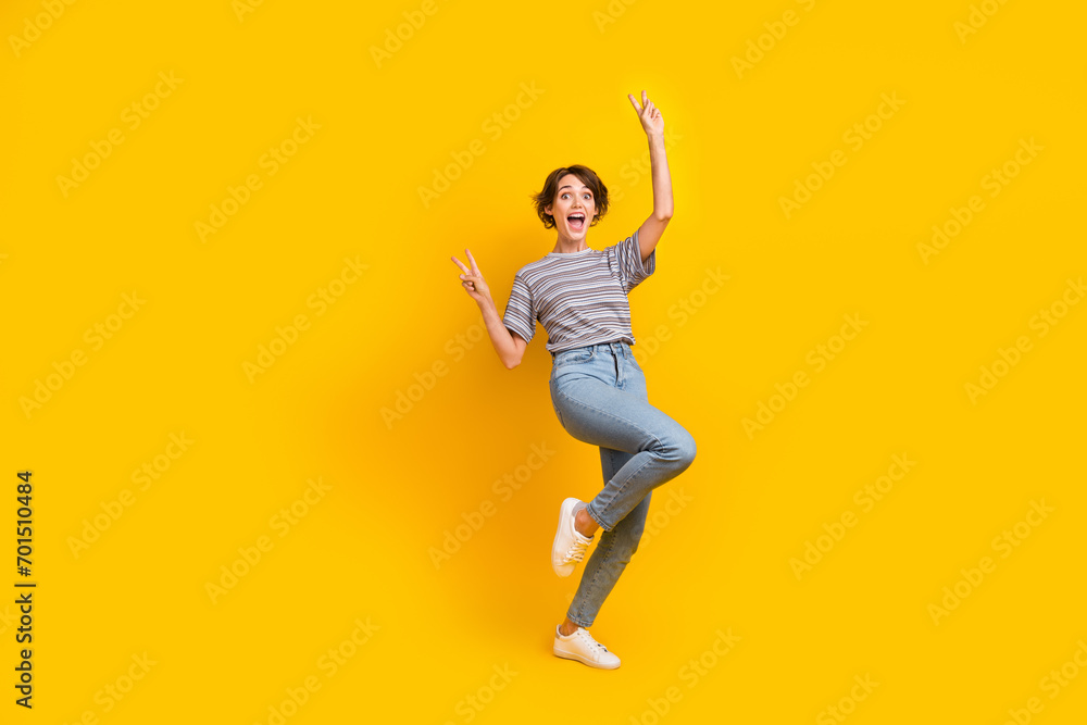 Full size photo of nice overjoyed astonished girl demonstrate v-sign empty space isolated on yellow color background