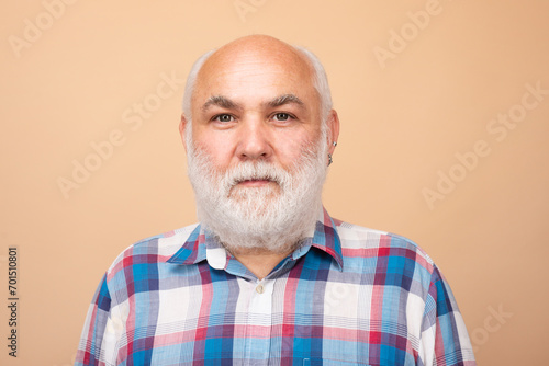 Face of 60s elderly retired mature aged pensioner. Portrait of an mature senior man with grey beard isolated on beige studio background.
