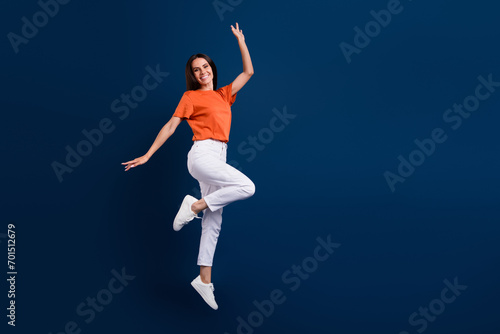 Full length photo of excited funky woman dressed orange t-shirt jumping high empty space isolated dark blue color background