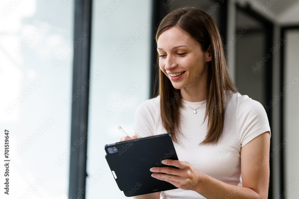 Fototapeta premium Caucasian university woman using a tablet with a stylus, with a laptop and phone nearby.