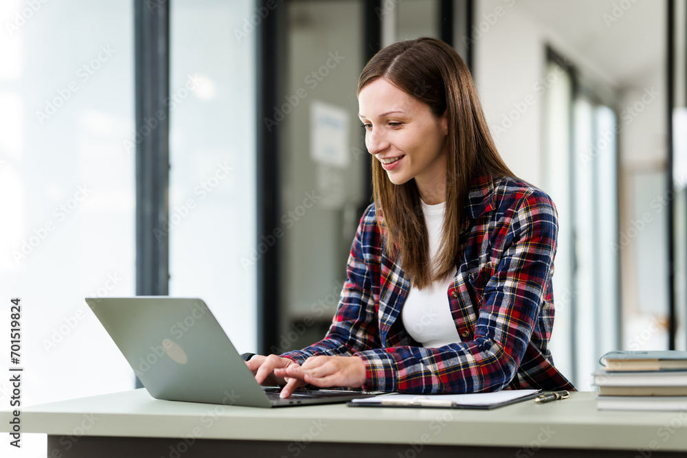 Caucasian university woman working on a project, with a laptop, clipboard in hand, and books on the table. Caucasian university woman working on a project, with a laptop, clipboard in hand, and books on the table.