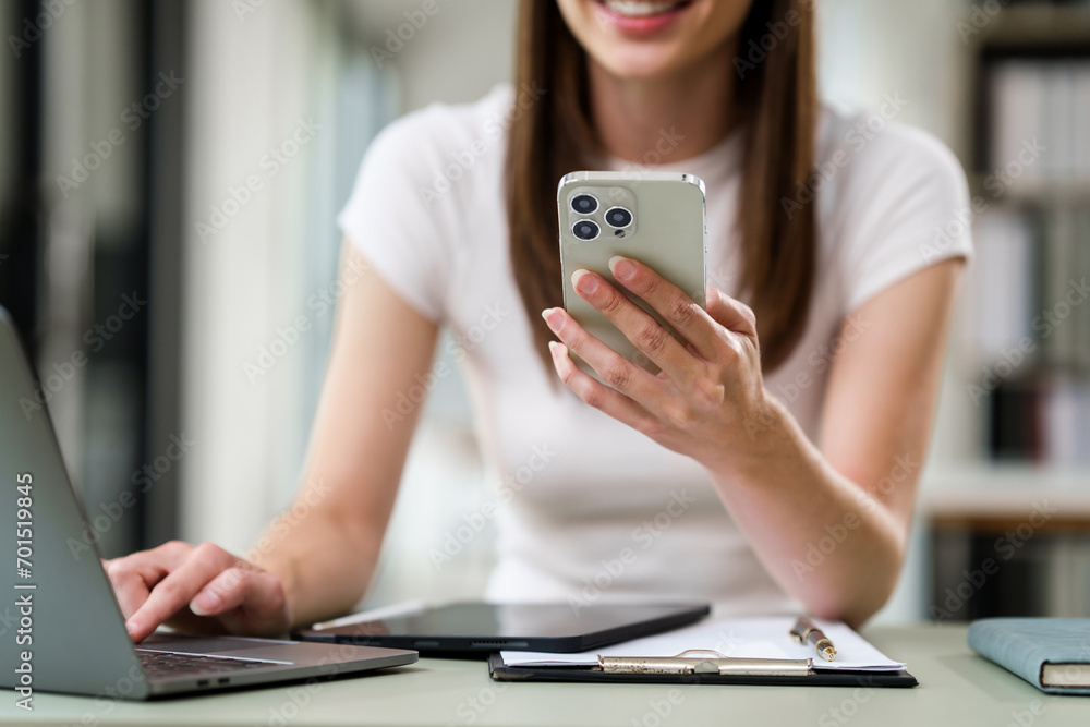 Caucasian university woman speaking into a smartphone with her hand near her mouth, a laptop in front of her.