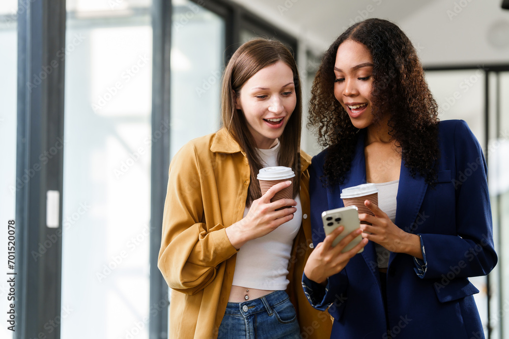 Caucasian and an African American university woman engaged in a conversation, holding a notebook and a coffee cup. Caucasian and an African American university woman engaged in a conversation, holding a notebook and a coffee cup.
