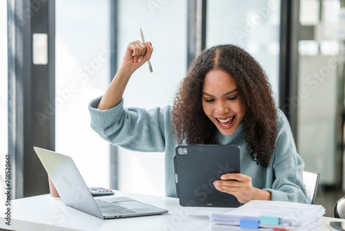elated African American university student, possibly celebrating a successful moment in her MBA project, holding a tablet and a pen aloft. photo