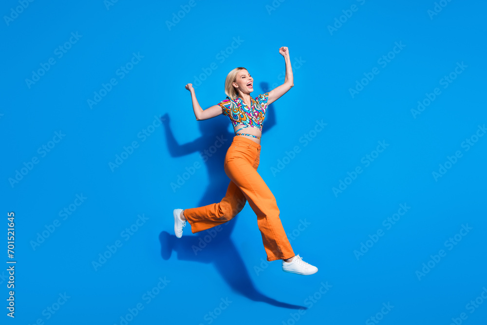 Full size photo of lovely overjoyed girl wear blouse orange trousers jumping win bet run to empty space isolated on blue color background