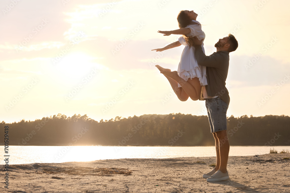 Fototapeta premium Happy couple dancing near river at sunset. Space for text