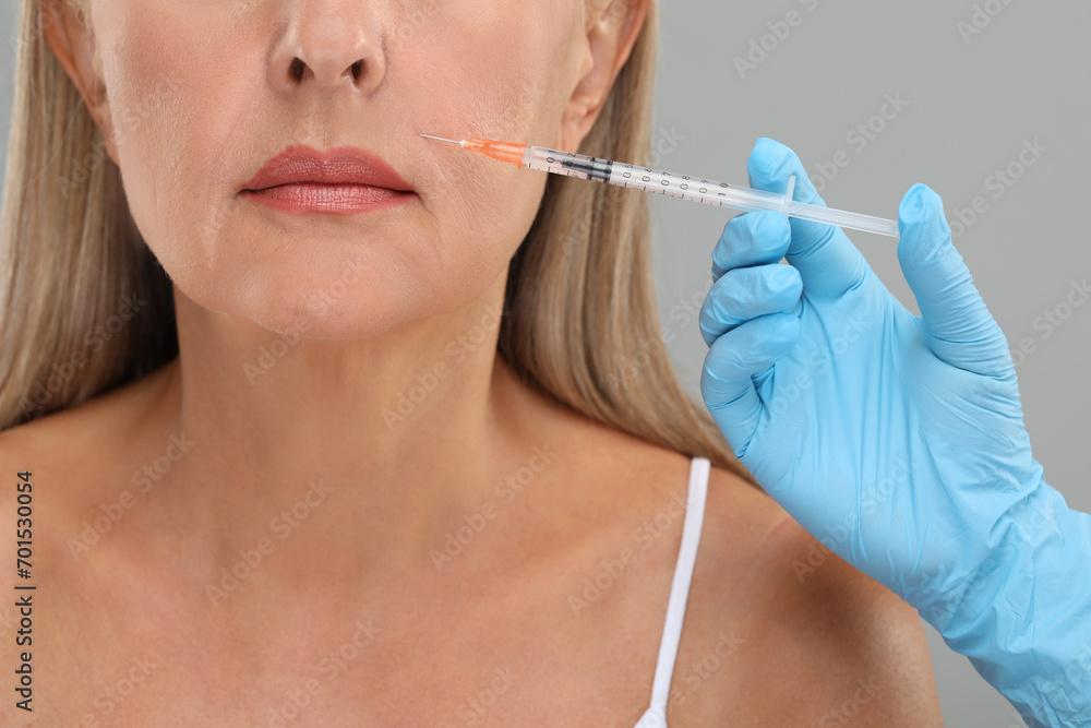 Doctor giving facial injection to senior woman on light grey background, closeup. Cosmetic surgery Doctor giving facial injection to senior woman on light grey background, closeup. Cosmetic surgery