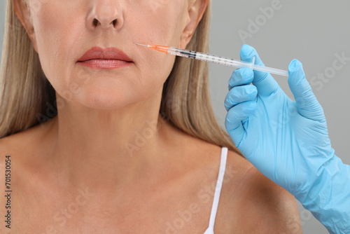 Doctor giving facial injection to senior woman on light grey background  closeup. Cosmetic surgery