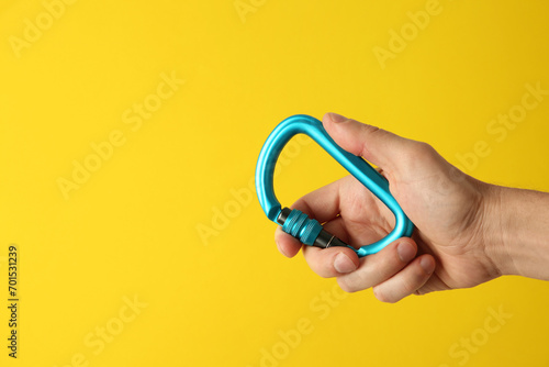 Man with metal carabiner on yellow background, closeup. Space for text
